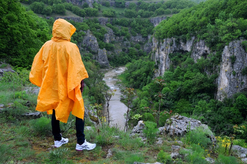 A woman in orange rain poncho stands on the edge of Emen canyon in Bulgaria on a raw foggy morning in the spring