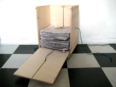 A DIY newspaper baler with the front hatch down and about half full of newspapers.