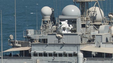Detail of the Laser Weapon System (LaWS) on the USS Ponce. The laser gun is a white cylinder on top of a gray ship.