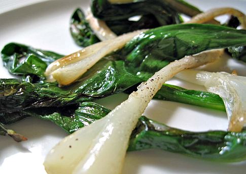 Some cooked ramps on a white plate.