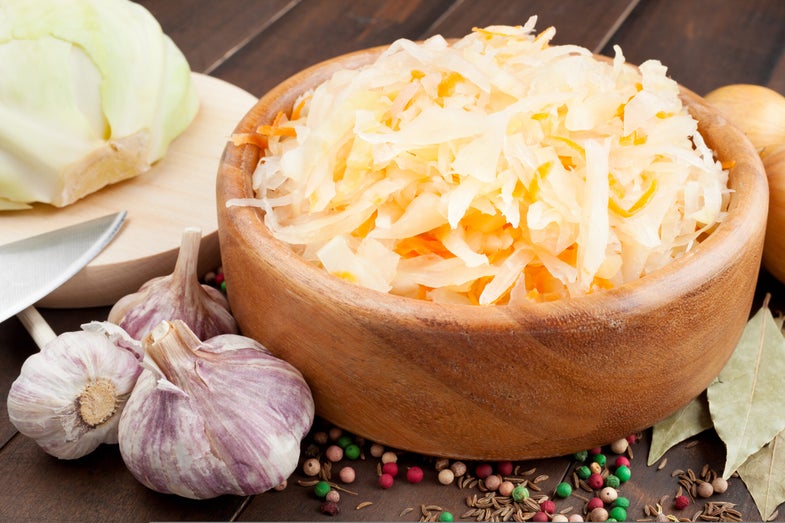 Sauerkraut with carrot in wooden bowl, garlic, spices, cabbage on a cutting board
