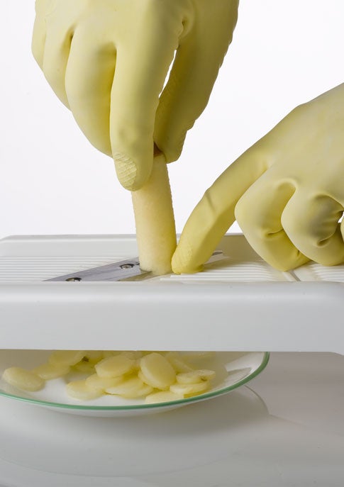 A person wearing yellow rubber gloves slicing an apple on a mandoline slicer.