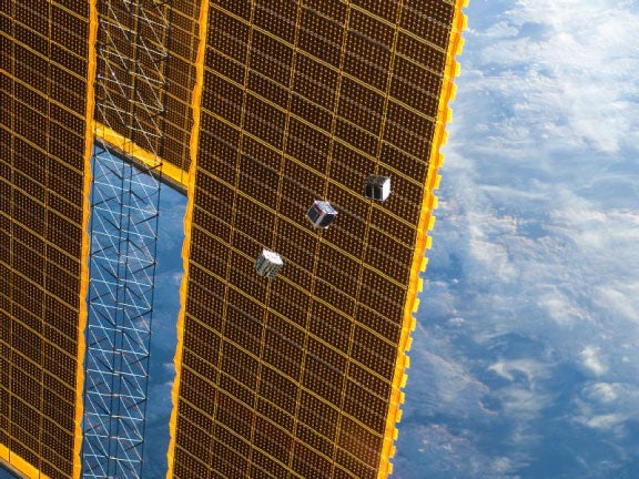Several small satellites drift away after being released from the Kibo Laboratory at the International Space Station. Some of the Station's solar panel arrays are visible in the background.