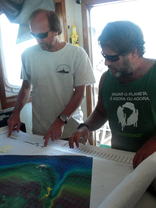 Researcher Steve Ross (left) and <em>Arctic Sunrise</em> captain Pete Willcox plot the course of the sub from the bridge with the help of a colorful sonar map showing known coral reef sites (pink and yellow areas).