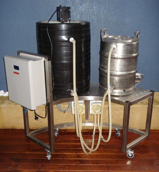 A beer brewing station made up of one large black keg in the center, a smaller silver one on the right, and a white electronics box on the left.