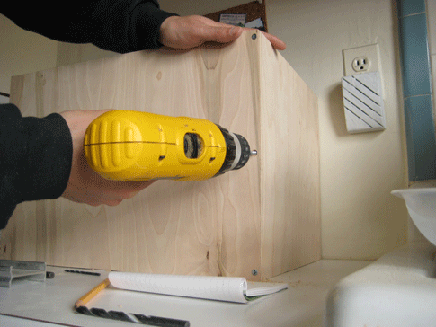 A person using a power drill to assemble sheets of plywood into a box.