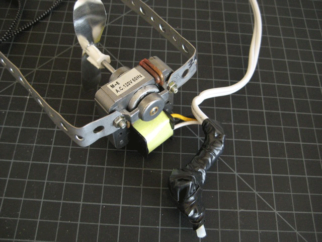 A motor and a bracket with an electrical power cord coming out of it.