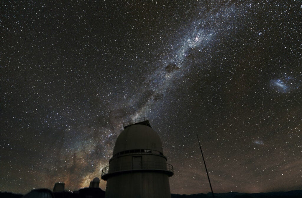The Milky Way seen above the dome of the Danish 1.54-metre telescope at ESO's La Silla Observatory in Chile, used to search for exoplanets using the microlensing technique. The central part of the Milky Way is visible behind the dome of the ESO 3.6-metre telescope; on the right, the Magellanic Clouds.