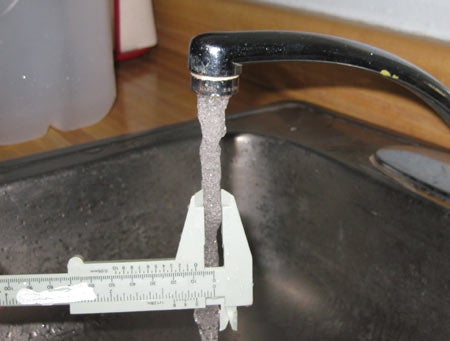 A normal stream of water coming out of a sink faucet. A person is measuring the stream width with calipers.