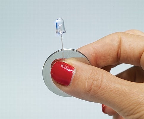 A person with red nail polish holding a small LED.