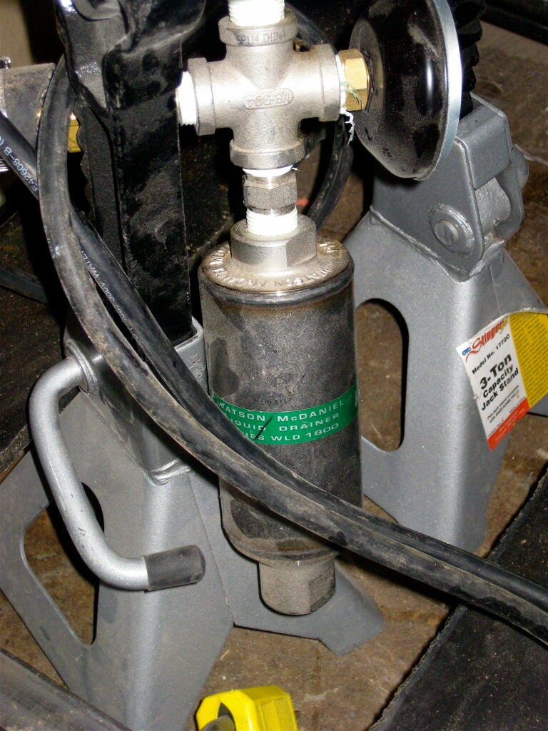 A sampling port is connected to the bottom of the white bucket that holds the yellow tubing (see previous picture), which collects the bio-oil and automatically empties it into a drip pan. Other re:char prototypes, like the Norfolk, Connecticut farm unit, use old water-cooler tanks to store the bio-oil.