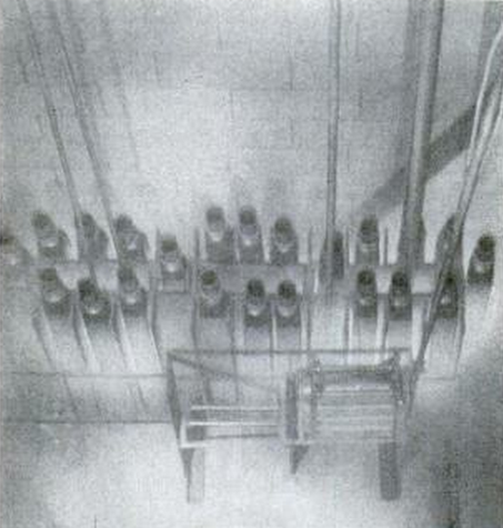 Revolving rack holding food in cans is lowered beside assembly.
