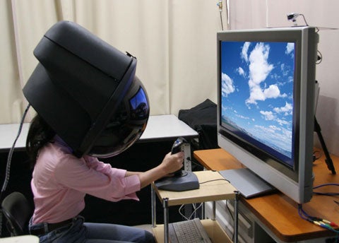 Is this the future of the home theater? No, it´s not a prop. This six-pound helmet monitor is a real prototype, built to demonstrate next-generation television-watching technology. Modeled here by one of its developers (the regular TV is shown only for comparison), the device was built by Toshiba and unveiled in September at an academic conference in Osaka, Japan. Equipped with a built-in projector and a dome screen, the monitor plugs directly into a DVD player or computer and provides an immersive experience that surrounds the wearer with the action of the program-think of it as a portable IMAX theater. Although the invention was popular among testers, who reported that it rests easily on the shoulders and is comfortable enough for a two-hour movie, Toshiba has no solid plans for commercialization.