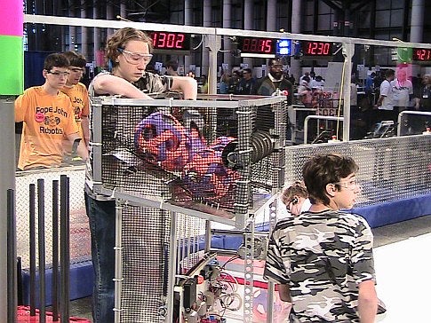Two high school students with a robot in an arena in front of a crowd at the 2009 FIRST Robotics Competition in New York City.