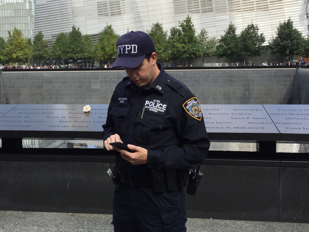 An NYPD officer using a smart phone in front of the World Trade Center memorial