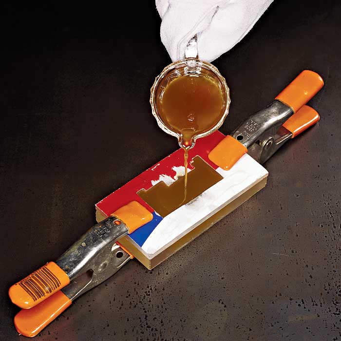 A person wearing white gloves pouring melted beeswax into a plastic mold held together by clamps.