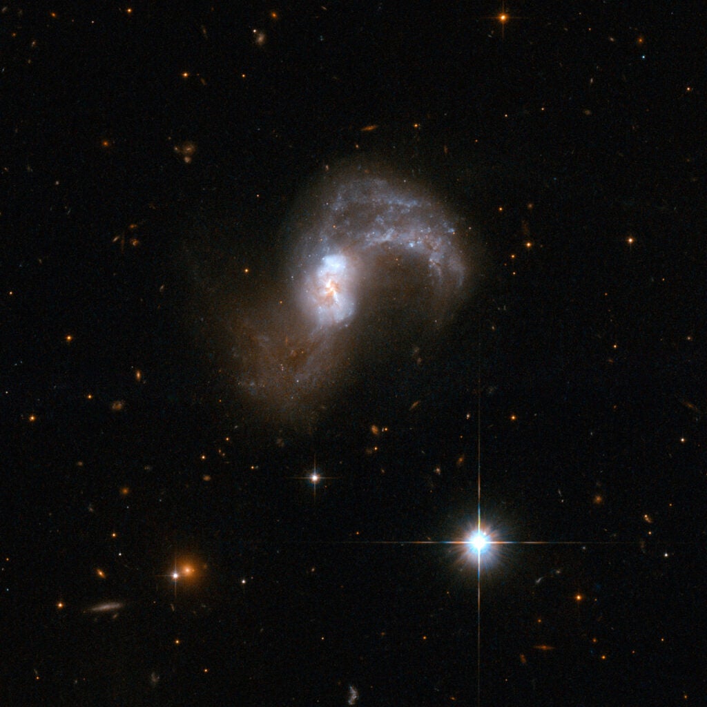 IC 2545 is a beautiful, but deceptive object that appears to be a single S-shaped galaxy, but is actually a pair of merging galaxies. The two cores of the parent galaxies are still visible in the central region. Other telltale markers for the collision include two pronounced tidal arms of gas and stars flung out from the central region. The tidal arm curving upwards and clockwise in the image contains a number of blue star clusters. IC 2545 glows strongly in the infrared part of the spectrum - another sign that it is a pair of merging galaxies. It lies in the constellation of Antlia, the Air Pump, some 450 million light-years away from Earth.