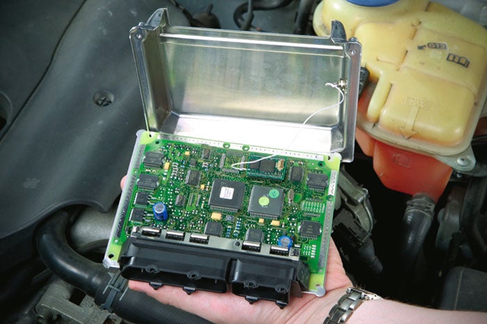 A person holding an engine control unit, or ECU, above the engine of a car.