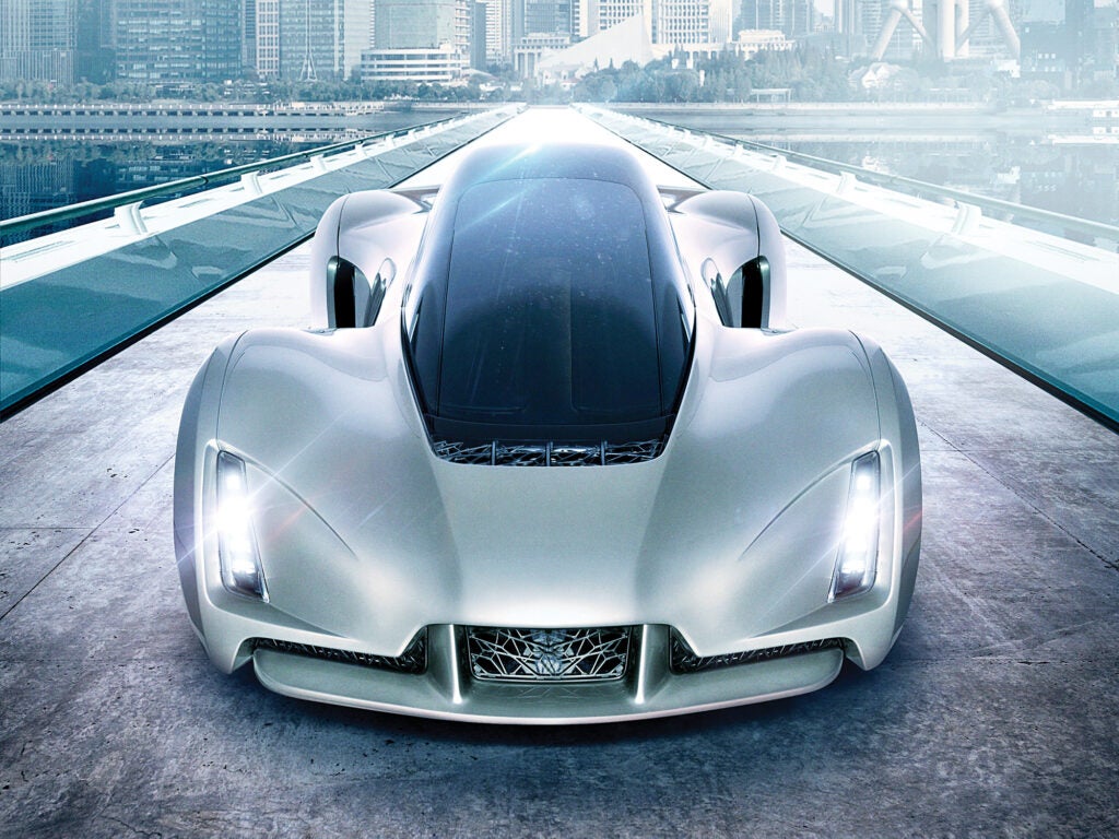 A head-on view of a slim silver sportscar with a cityscape in the background