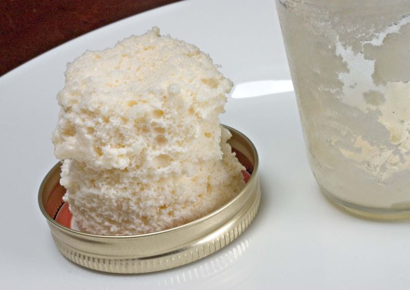 Brie cheese that has been aerated, sitting as a tower of foam in a metal dish on a white plate.