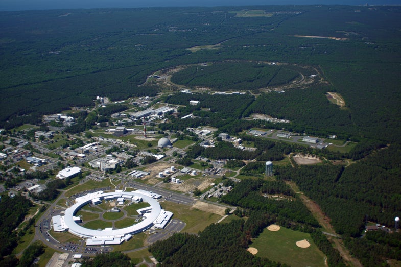 This aerial photo shows the white, circular National Synchrotron Light Source-II under construction in 2013. In the background is another circular accelerator, the Relativistic Heavy Ion Collider, which opened in 2000. RHIC is for studying conditions after the Big Bang.