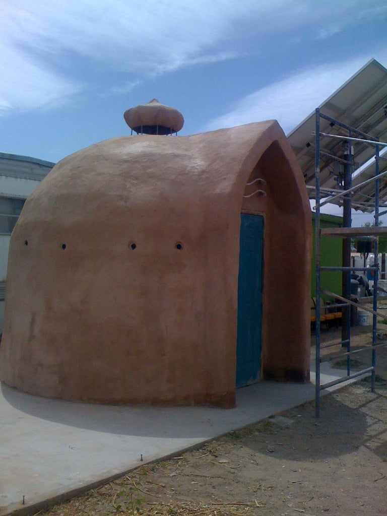 A brown domed structure with a blue door and a vent on the roof.