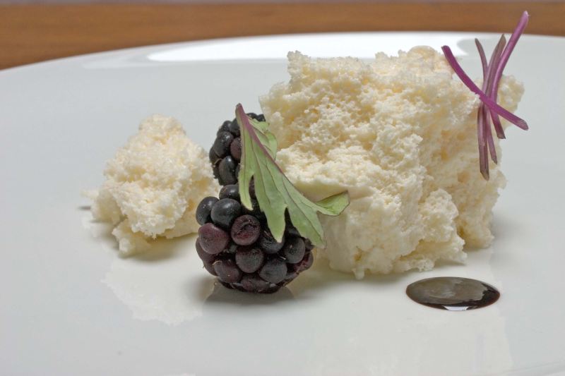 A large blob of aerated Brie next to a smaller chunk of it and some blackberries, on a white plate.