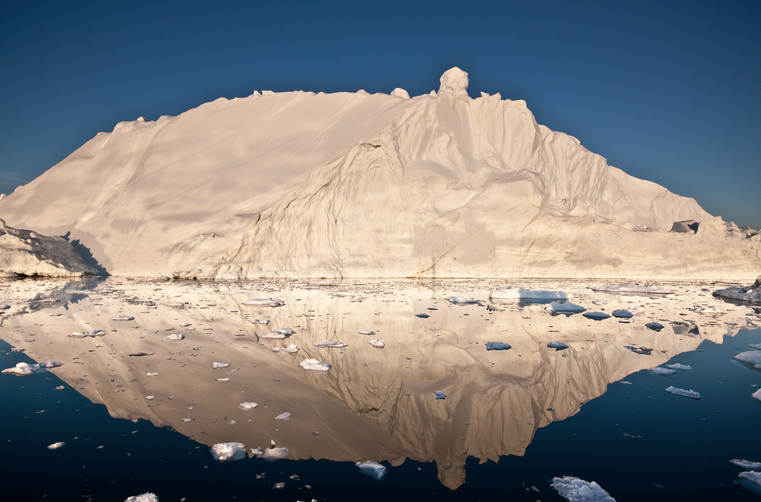 The midnight sun casts a golden glow on an iceberg and its reflection in Disko Bay, Greenland. Much of Greenland's annual mass loss occurs through calving of icebergs such as this.
