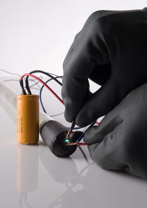 A person wearing black rubber gloves connecting wires to a battery made out of fruit.