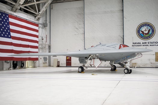 The X-47B drone in an aircraft hangar with the USA flag in the background