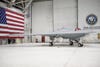 The X-47B drone in an aircraft hangar with the USA flag in the background