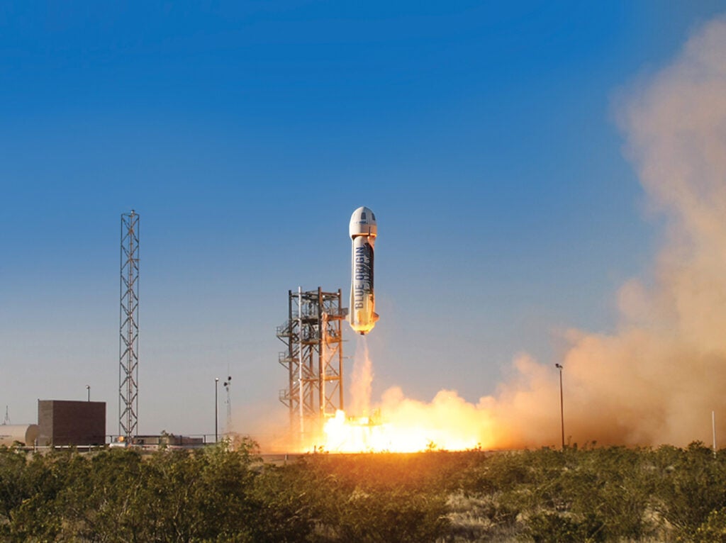 A stocky little rocket is taking off from a launch pad against a clear blue sky