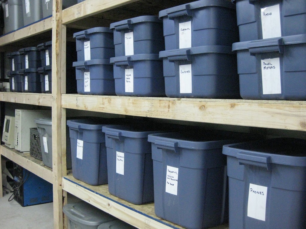 Shelves full of blue Rubbermaid Roughneck containers. The bottom shelf has large 18-gallon containers, and the shelf above that has double-stacked 10-gallon containers.