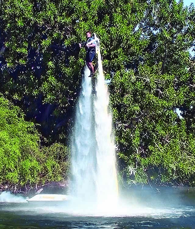 A man hovering about 20 feet in the air above a small body of water while using a water-powered jetpack.