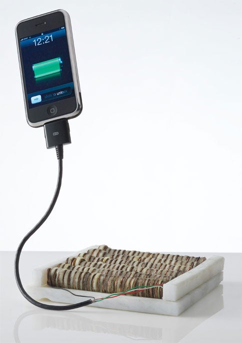 An iPhone plugged into a battery made out of apples and pennies.