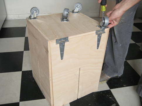 A person attaching wheels to the underside of a homemade newspaper baler.