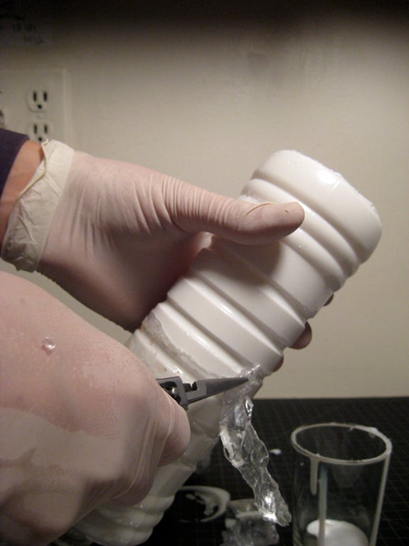 A person removing a plastic bottle from around a plastic mold.