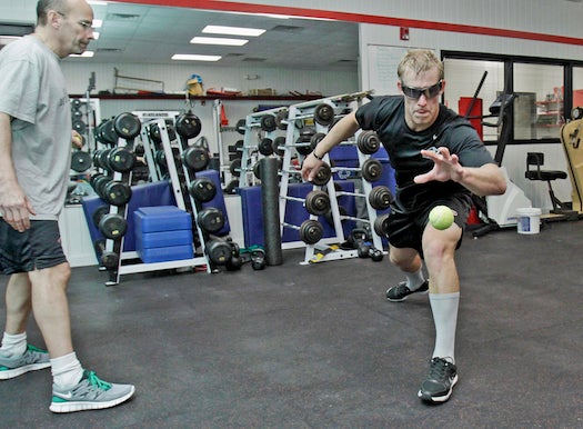 The Carolina Hurricanes' Justin Peters, right, lunges for a ball that trainer Pete Friesen, left throws to him at Raleigh Center Ice in Raleigh, N.C. on Aug. 31, 2011. Friesen has been using the Nike strobe goggles that Peters is wearing to help develop the players' vision and response time.