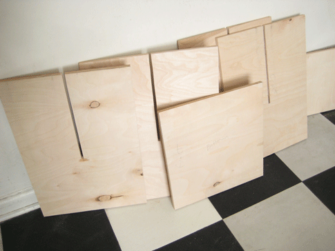 Several sheets of plywood against a wall on a tile floor.