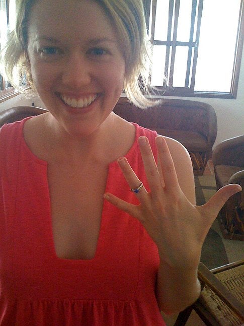 A blonde woman wearing a red dress and showing off an engagement ring.