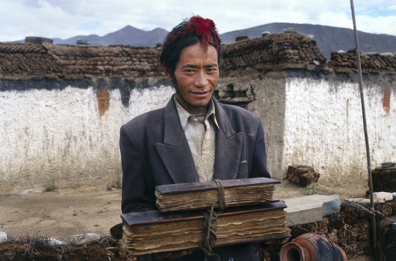This photograph shows a Tibetan doctor standing on the roof of his house holding two precious medical books. One is a copy of the fundamental Tibetan medical classic Gyu Shi ('Four Tantras') written in the 12th century; the other is a manuscript on compounding medicines, which was composed by the members of his medical family (going back four generations) and takes into account the knowledge the doctors of this lineage have gained through trial and error. The photo was taken in the Tibetan Autonomous Region, China, in 2003. [<a href="http://www.wellcomeimageawards.org">Wellcome Image Awards</a>]