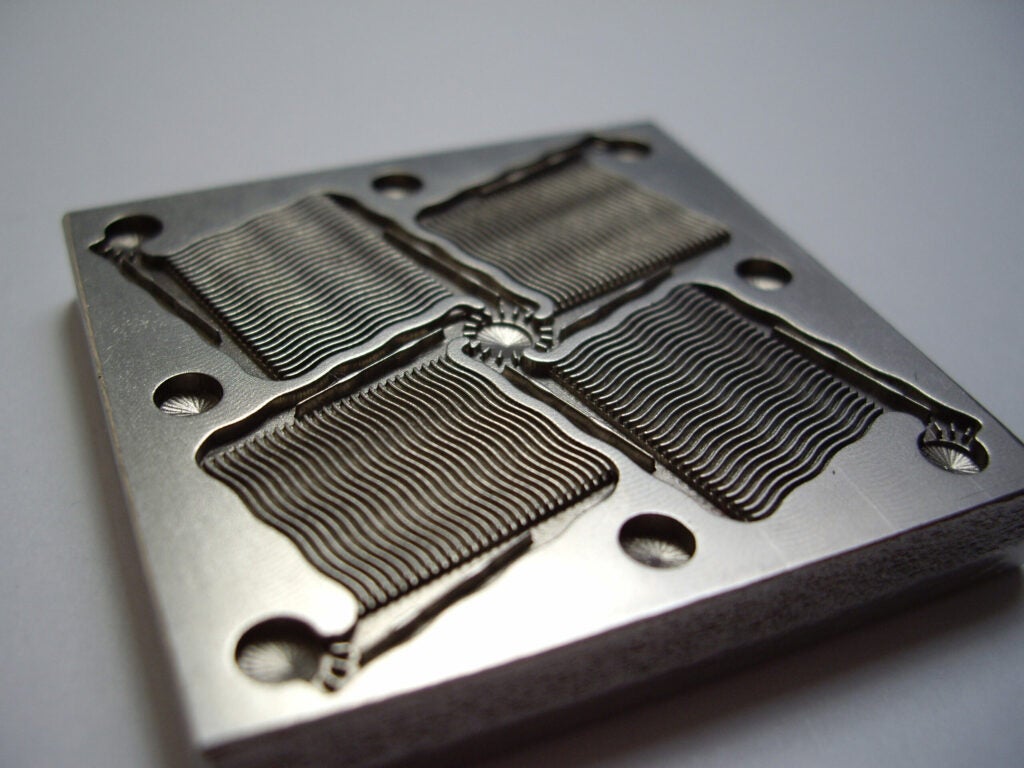 A square piece of metal with detailed shapes etched onto it via electrochemical machining.