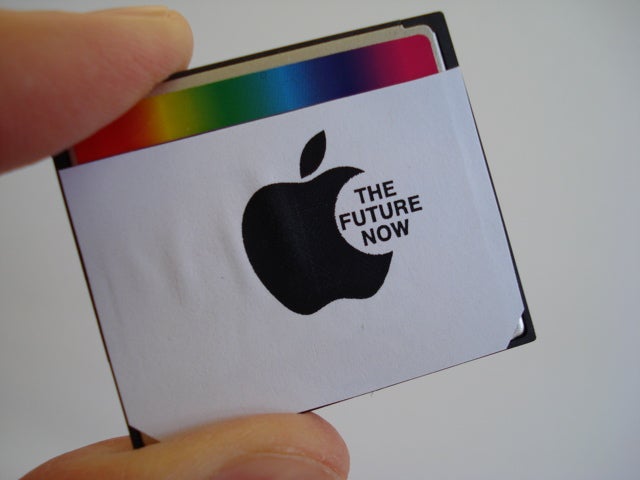 A person holding a small device with an Apple sticker that says "the future now."