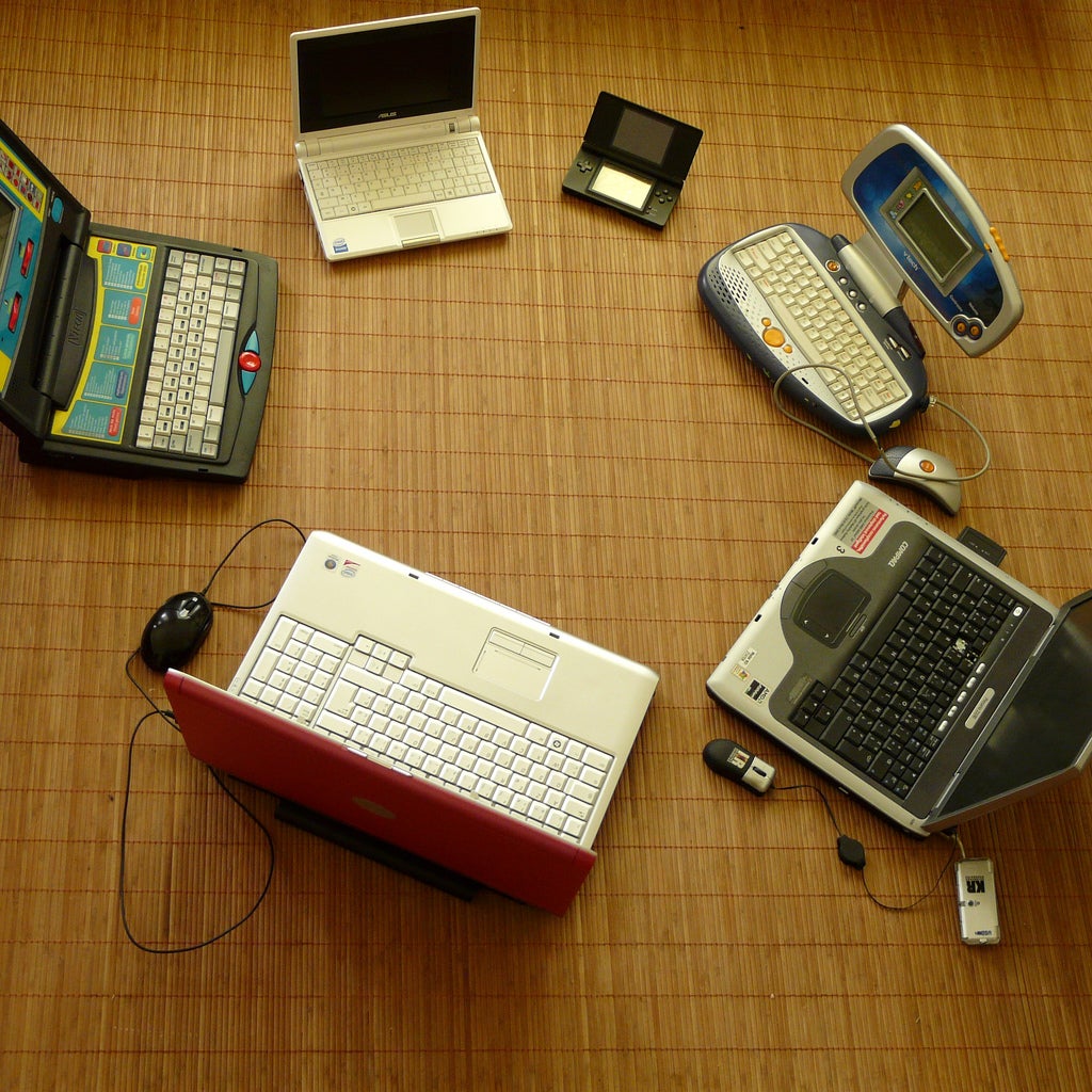 Four laptops of varying sizes, plus two smaller devices, in a circle on a wooden floor.
