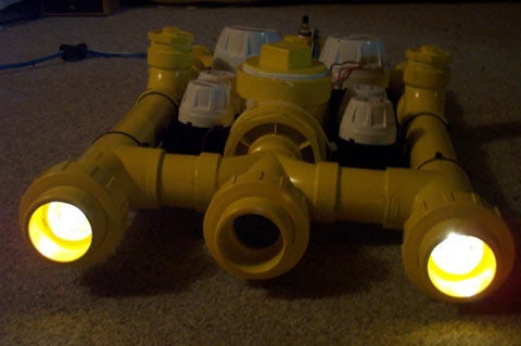 A yellow homemade ROV on the ground with its lights on.