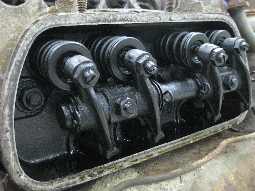 After the fuel-air mixture travels down the intake manifold, it arrives at the cylinder head. It ultimately needs to end up inside the cylinder, but only at the right time. Shown here are the rockers and the valves. The rocker arms depress the spring-loaded valves, opening them to allow the intake charge to enter at precisely correct moment and, slightly later in the cycle, to allow the exhaust gases to leave.