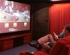 A person sitting in a red theater room watching a poker game on a large TV.
