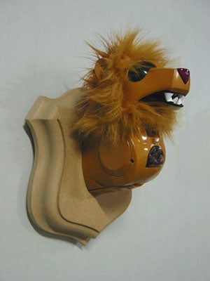 A robot lion head mounted as a hunting trophy on a white wall.