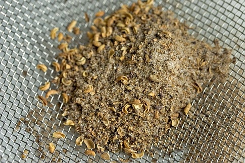 A pile of tan Szechuan salt in a strainer.
