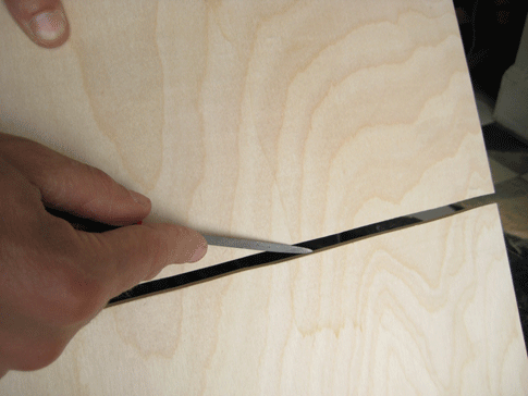 A person cutting a slit in a piece of plywood.